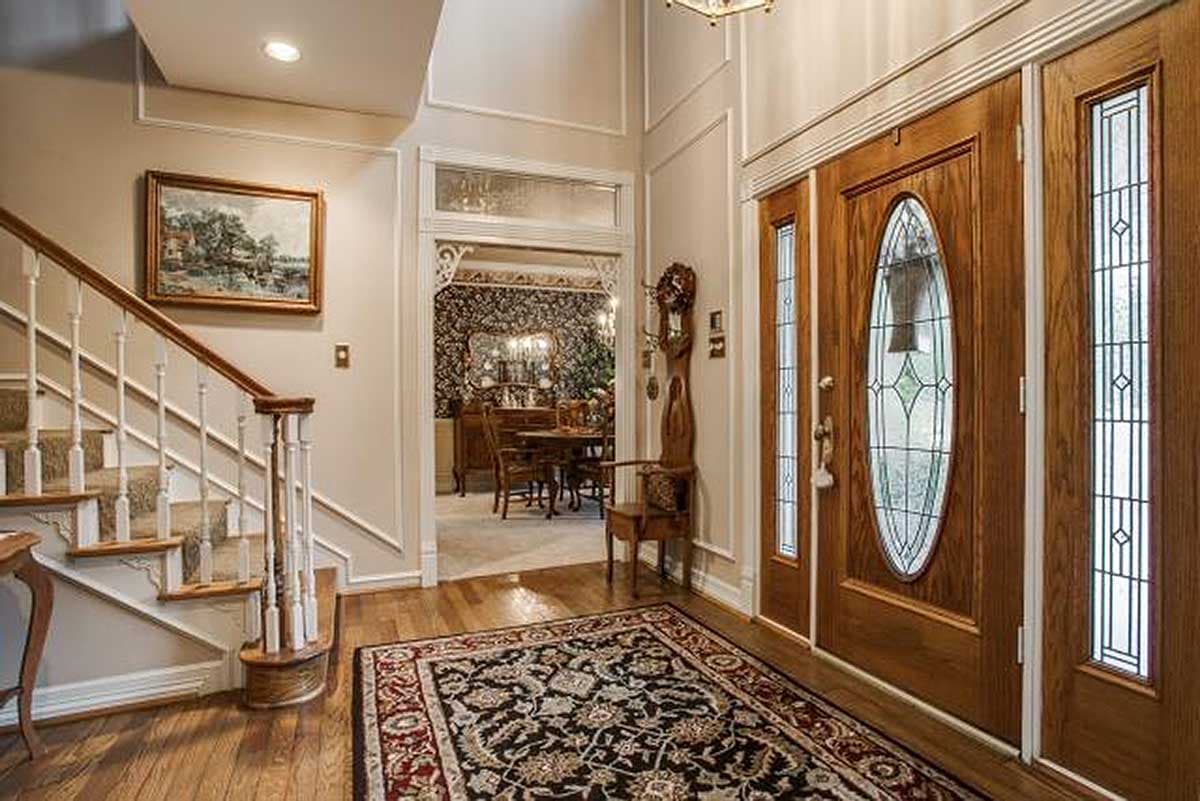Entryway with carpeted staircase, wood flooring, ornate rug, and double wood doors with leaded glass sidelights.