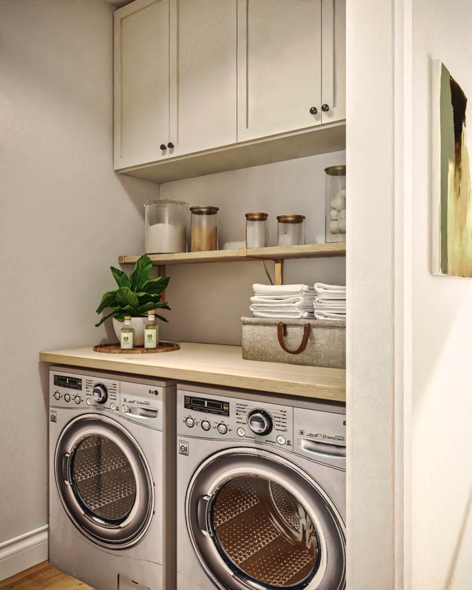 A modern laundry room with two silver washing machines, a wooden countertop, shelves, and cabinets. A decorative plant and folded towels are visible.