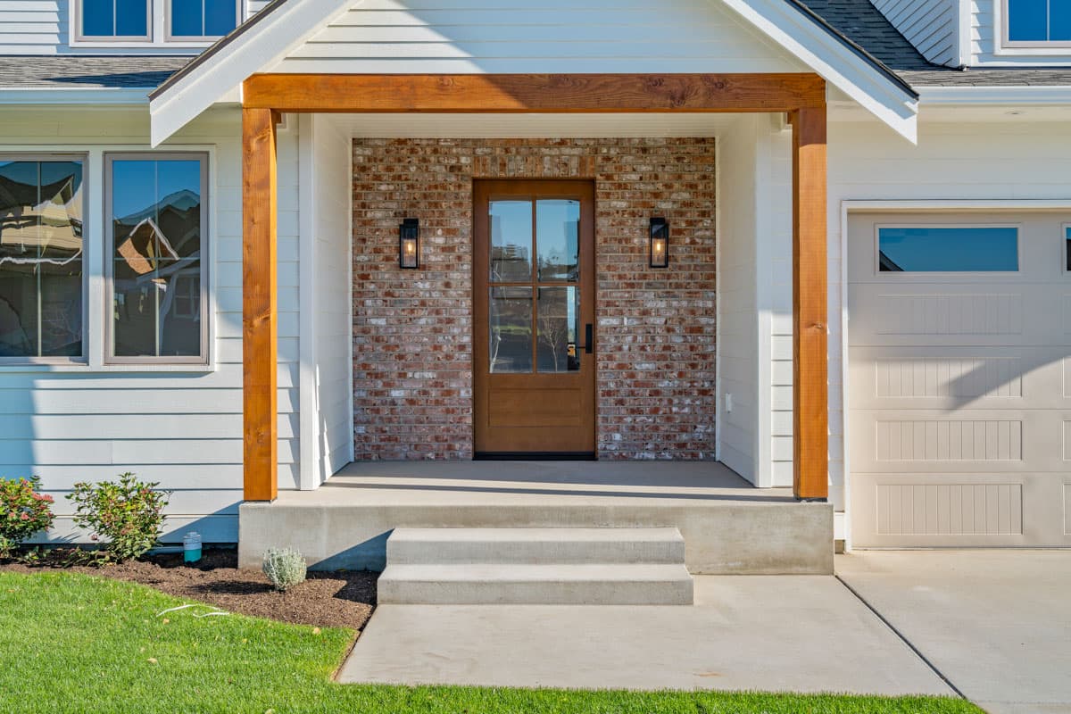 Modern Farmhouse house plan exterior with wood-framed covered porch, brick accent wall, wood door, and attached garage.