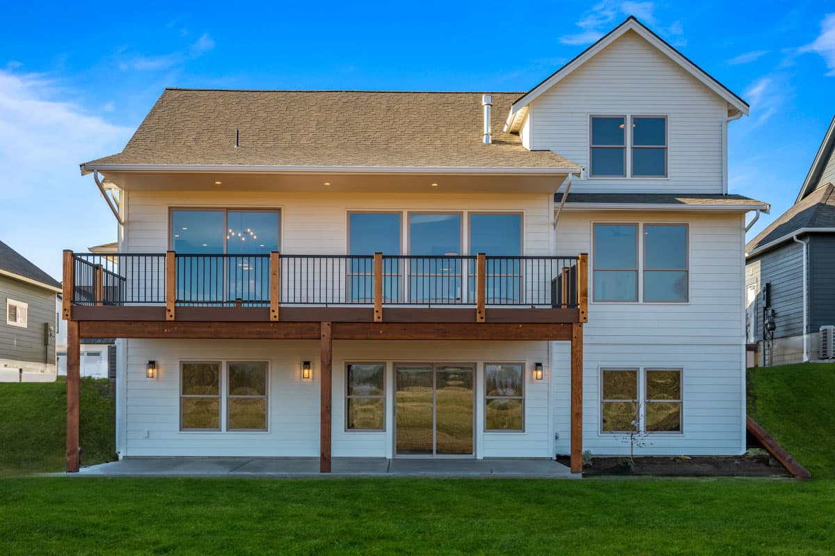 House plan exterior: Two-story white siding home with a large elevated deck, gabled roof, and numerous large windows.