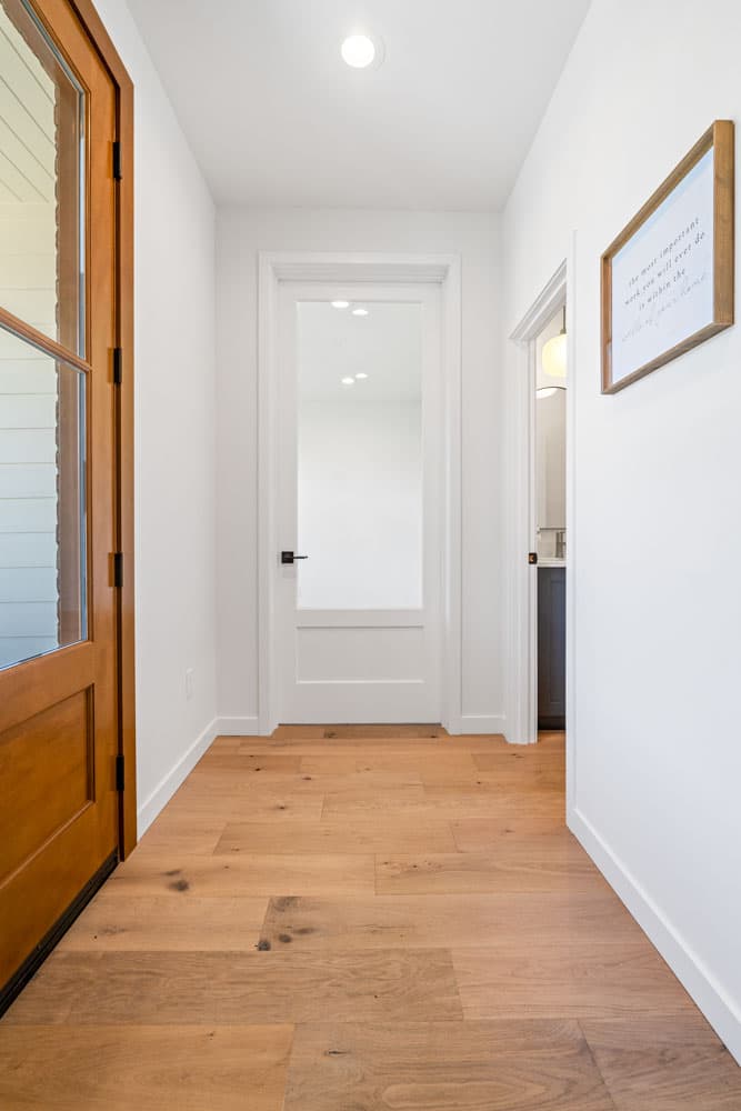 Hallway interior with wood floors, glass-paneled door, and framed wall art.