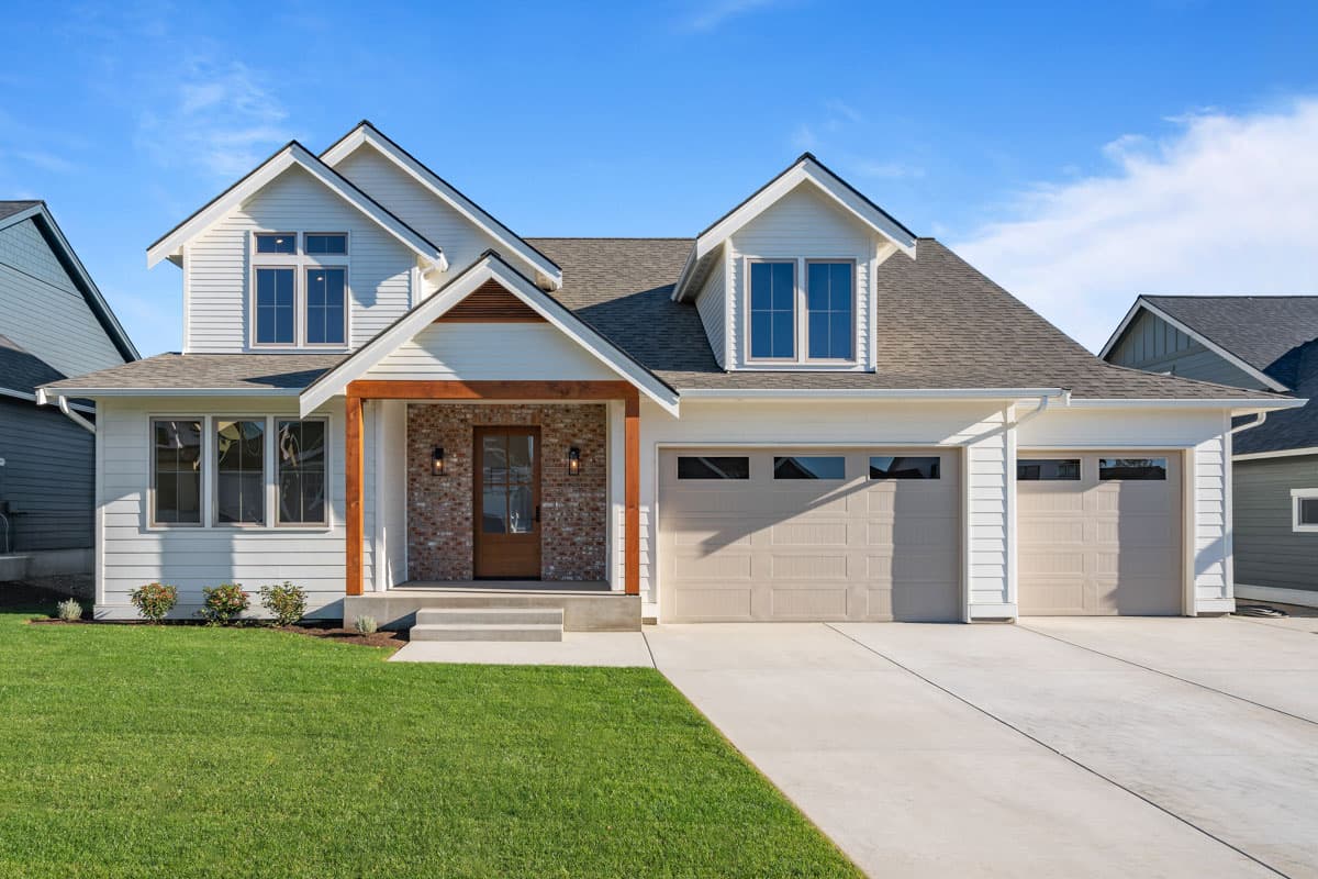 House plan exterior. Two-story, farmhouse style home with gabled roof, dormers, and front porch with brick accent. Attached garage.