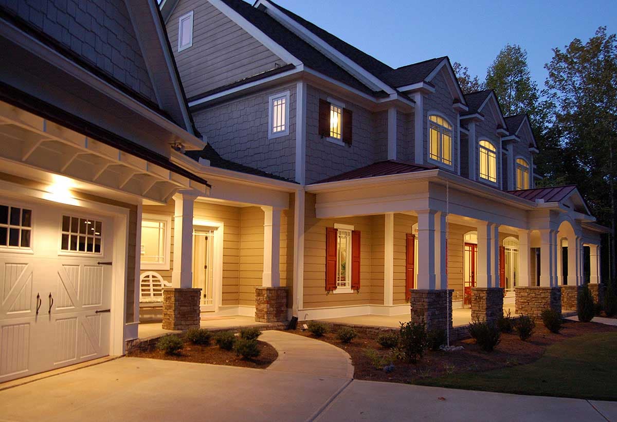 Two-story house plan exterior with a wide covered porch, stone-clad columns, dormers, and a side-entry garage.