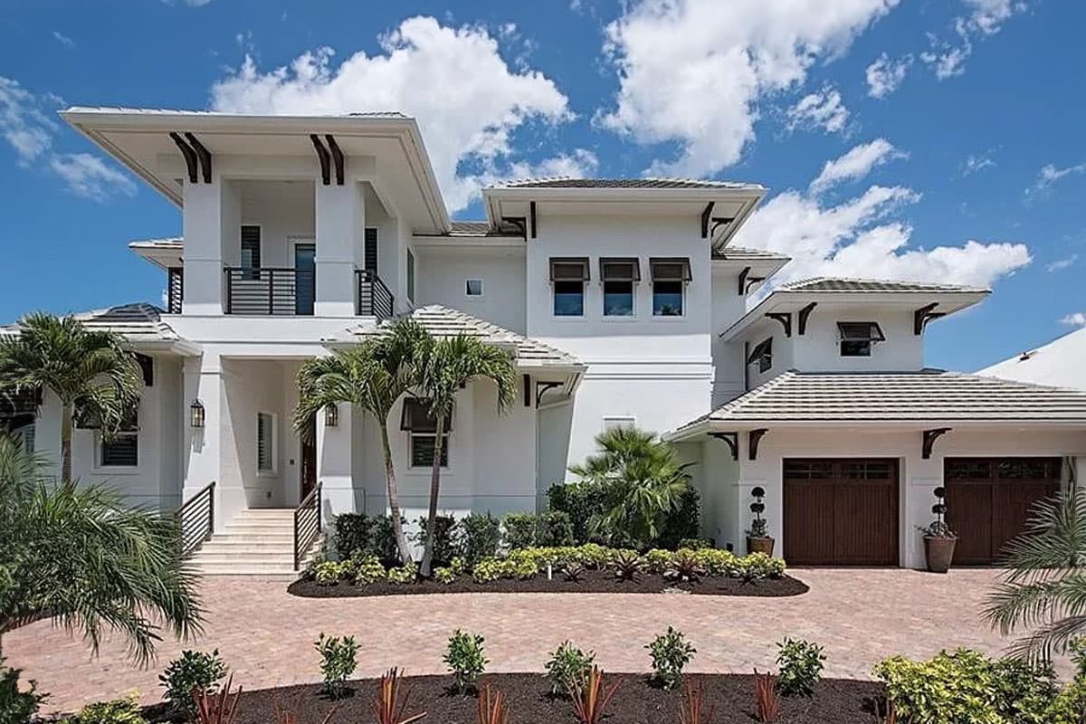 House plan exterior. Two-story, white stucco coastal home with overhanging rooflines, dark wood garage doors, and a second-story balcony.