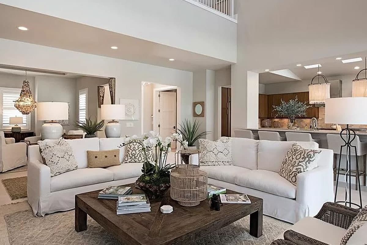 Interior view of great room with vaulted ceiling, open layout to kitchen, and white slipcovered sofas.