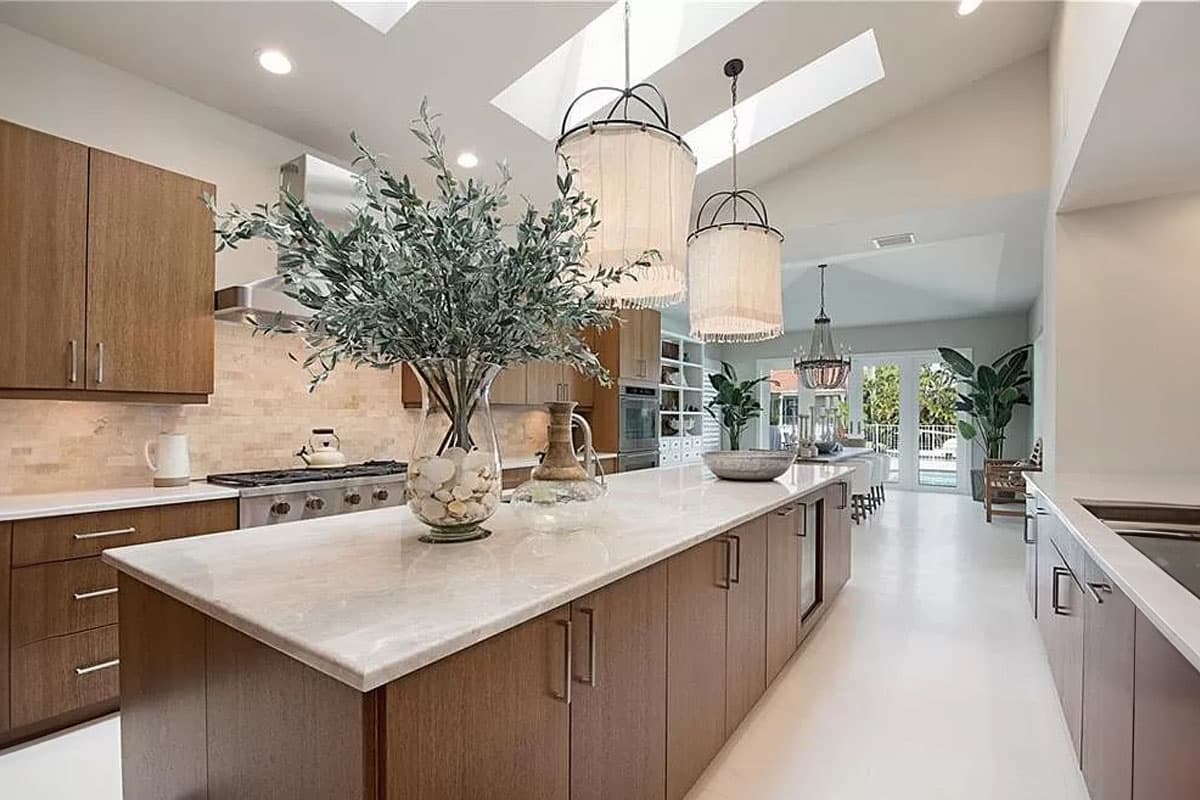 Modern kitchen with vaulted ceiling, skylights, large island, wood cabinetry, and view of dining area and pool.
