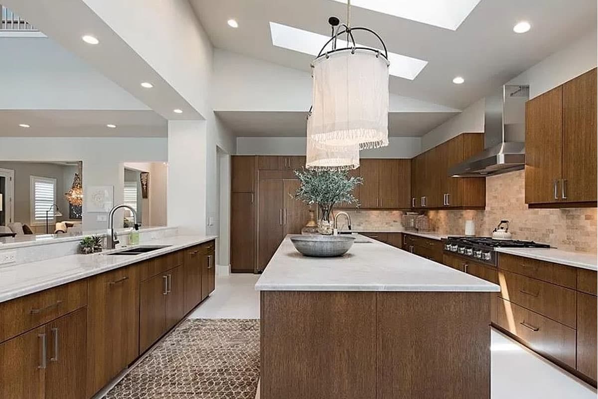 Modern kitchen with wood cabinetry, a large island with sink, stainless steel range hood, and skylights.