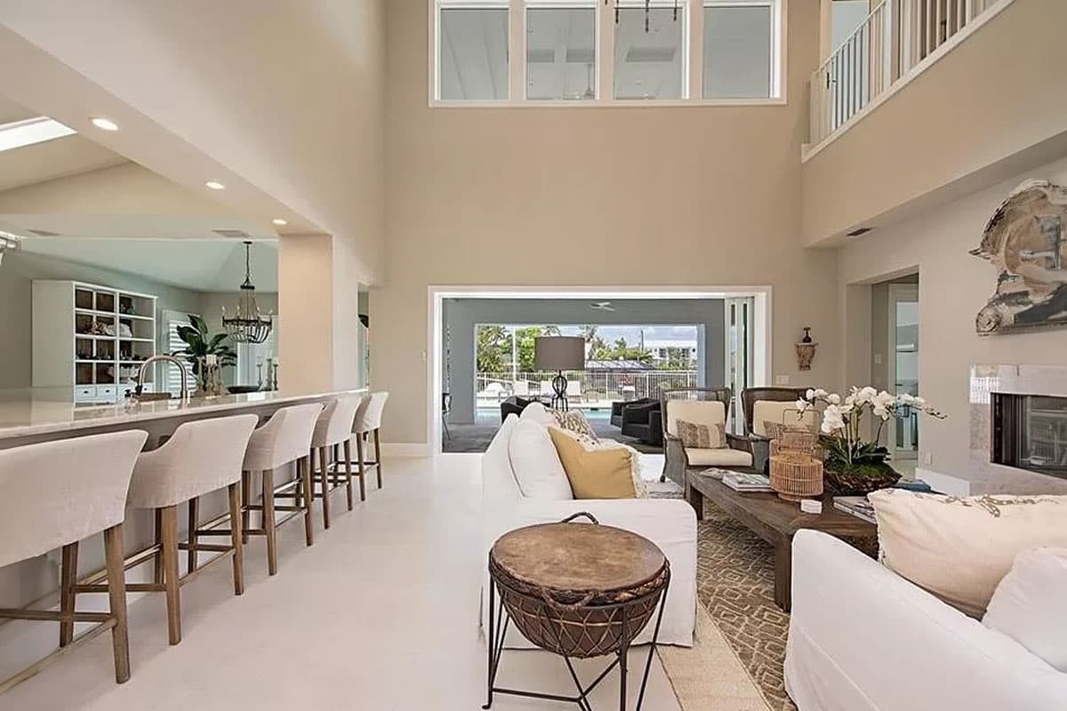 Interior view of a great room with a large kitchen island, vaulted ceiling, fireplace, and open access to an outdoor pool area.