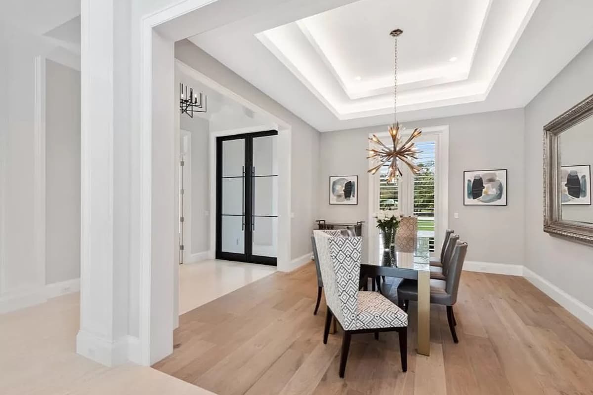 Interior dining room with coffered ceiling, black double doors, dining table and chairs, and large window.