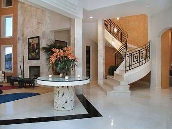 Interior view of a foyer with a white marble spiral staircase featuring decorative metal railings and a large fireplace.