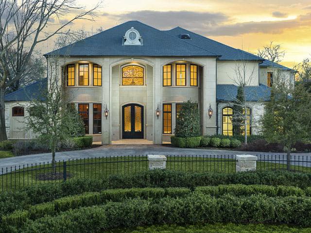 Two-story house plan exterior with light stone facade, arched windows, decorative window above double doors, and hipped roof.