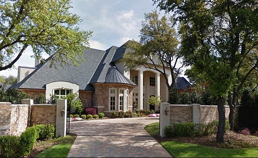 House plan exterior. Two-story home with a hipped roof, brick and stone facade, rounded turret, and prominent columns supporting a portico.