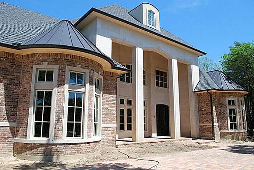 House plan exterior showing brick facade, quoins, bay windows, arched portico with columns, and conical roof elements.
