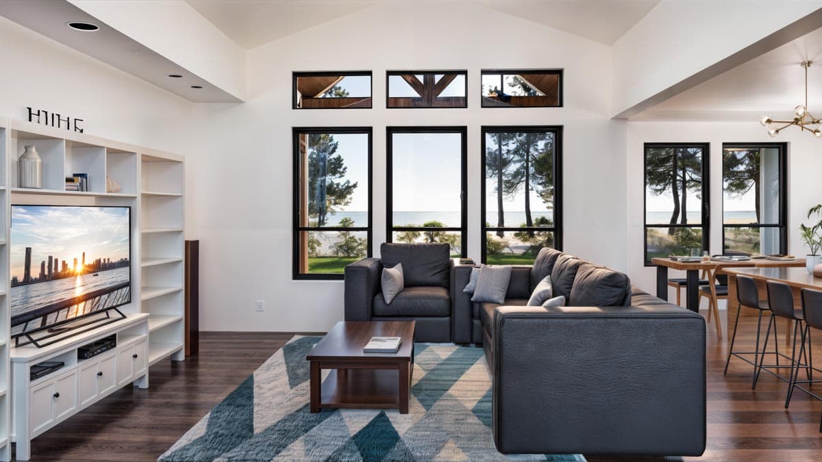 Interior view of a living room with a vaulted ceiling, large windows overlooking the water, a sectional sofa, and a built-in entertainment center.