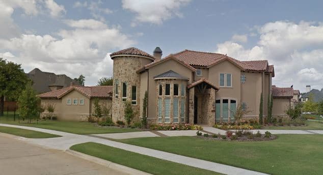 House plan exterior with a rounded stone tower, tile roof, multiple gables, and an arched entryway with stone accents.
