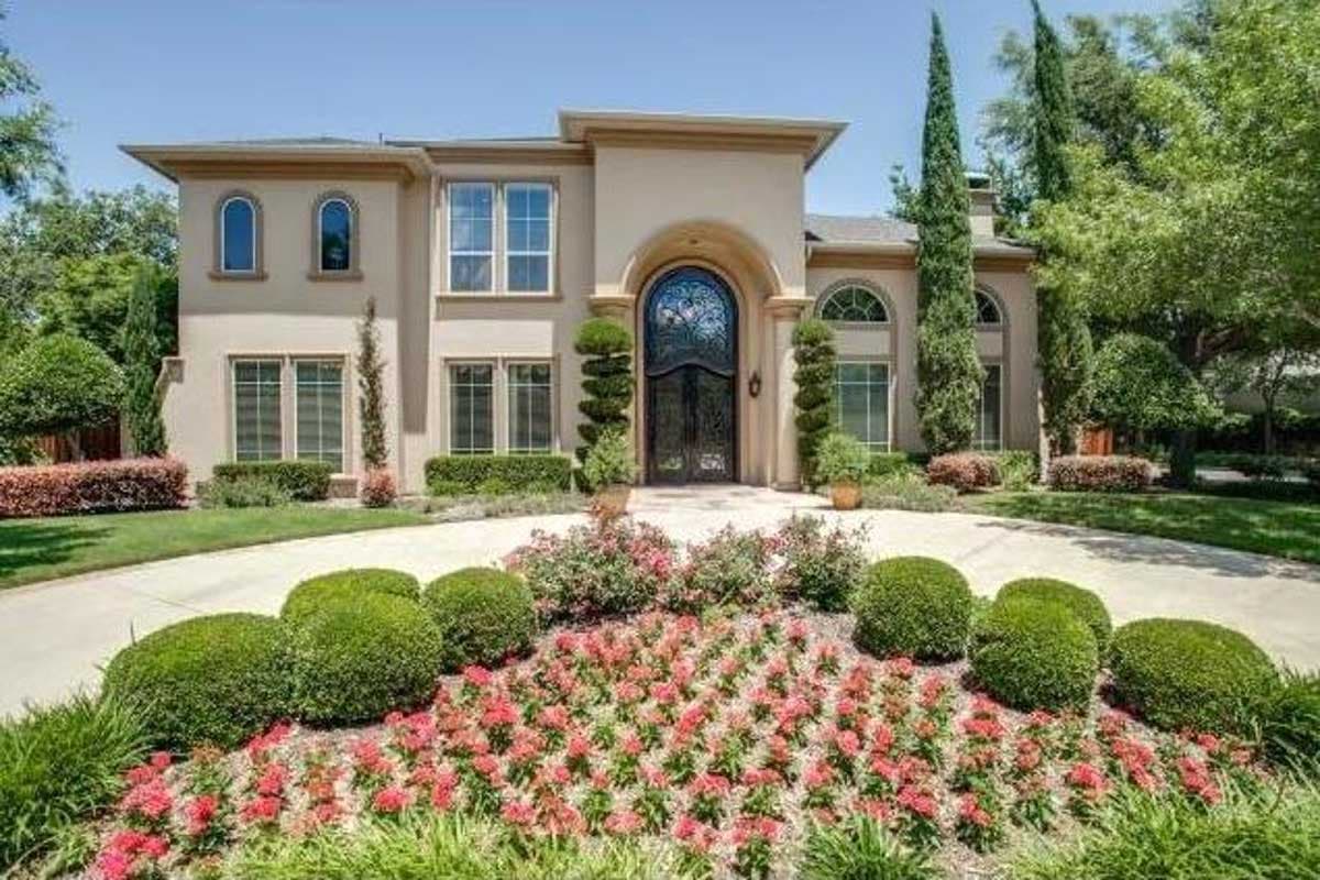 House plan exterior. Two-story Mediterranean style with arched entryway, arched windows, and multi-paned windows. Landscaping in foreground.