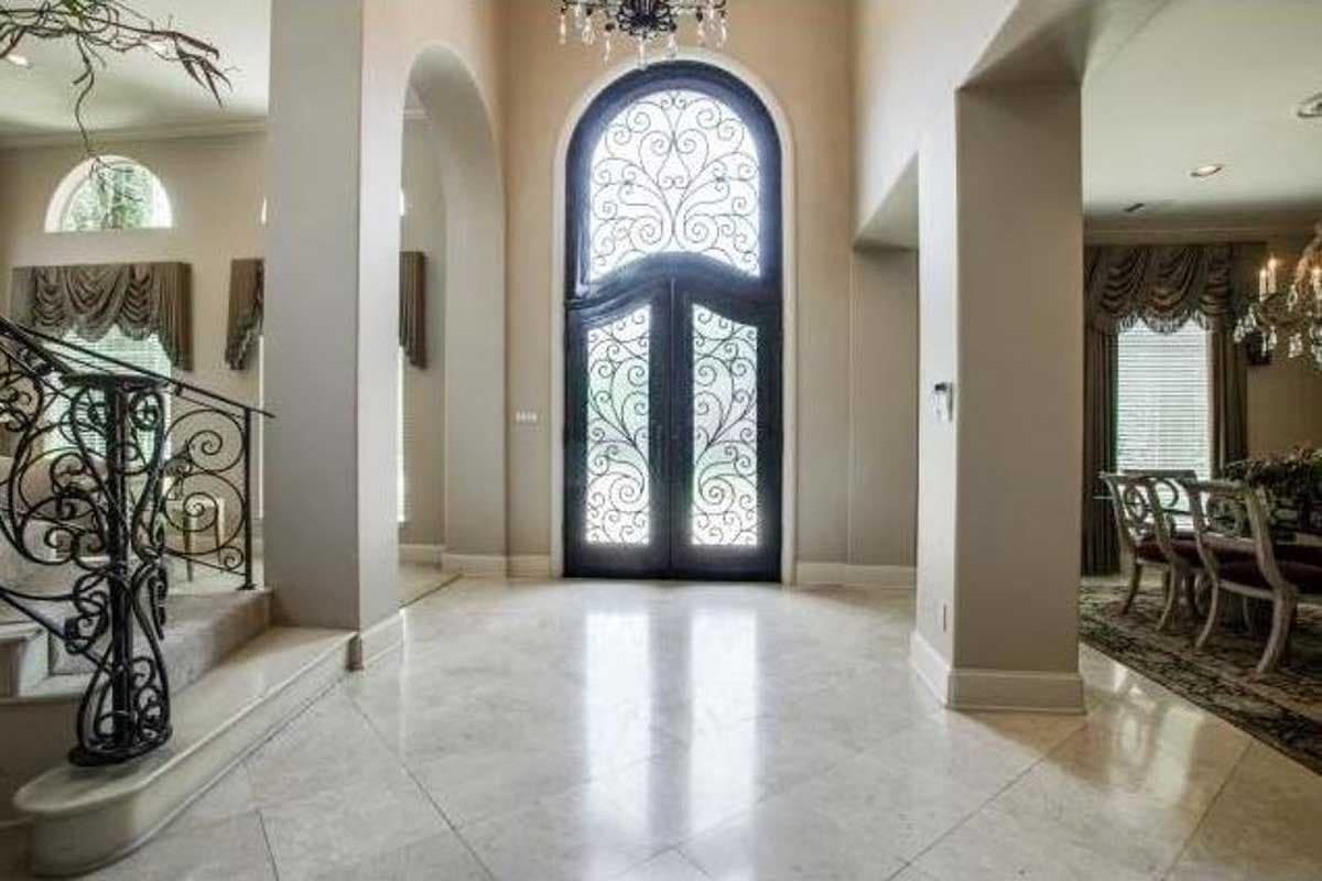 Entryway features double doors with arched transom and wrought iron detailing, marble flooring, and a grand staircase with ornate railing.