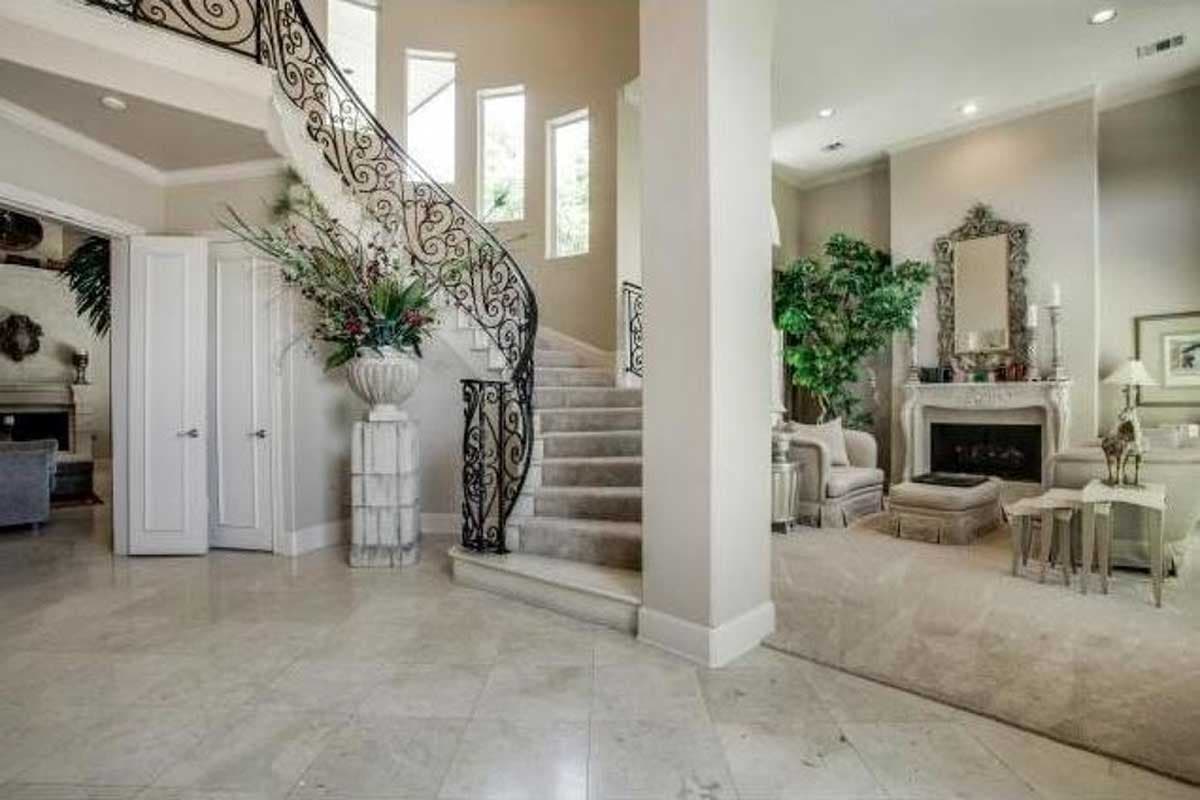 Interior view showing a grand staircase with ornate railings, a fireplace, and an open living area.