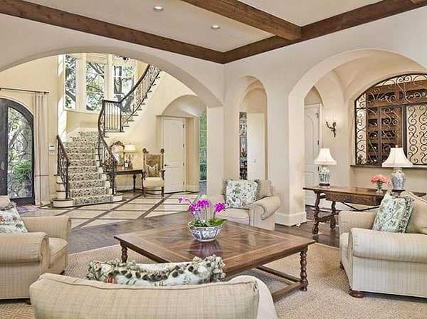 Interior view of a house with a grand staircase, arched doorways, wood beams, and patterned flooring.