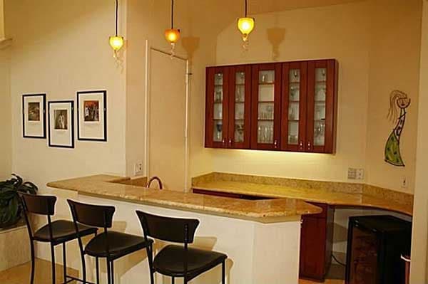 Bar area with granite countertop, wood cabinets with glass doors, pendant lights, and bar stools.
