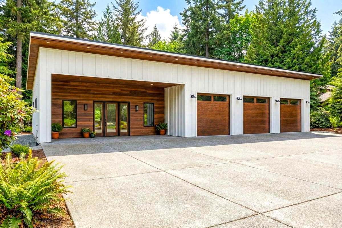 House plan exterior with modern style, flat roof, wood siding accent, three garage doors, and a covered entry.