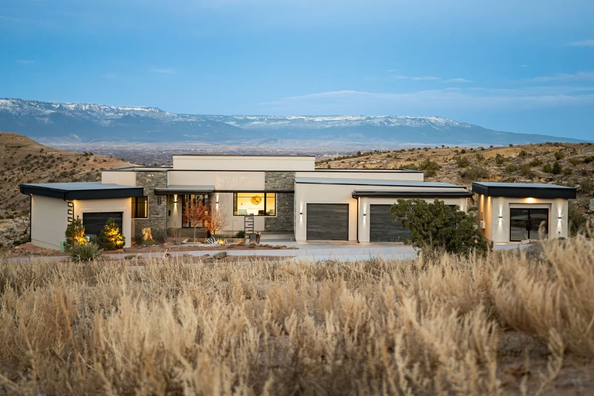 Modern house plan exterior with multiple garage doors, stone accents, flat rooflines, and panoramic mountain views.