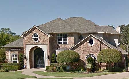 House plan exterior: two-story brick home with arched entryway, oval dormer windows, and varied rooflines.