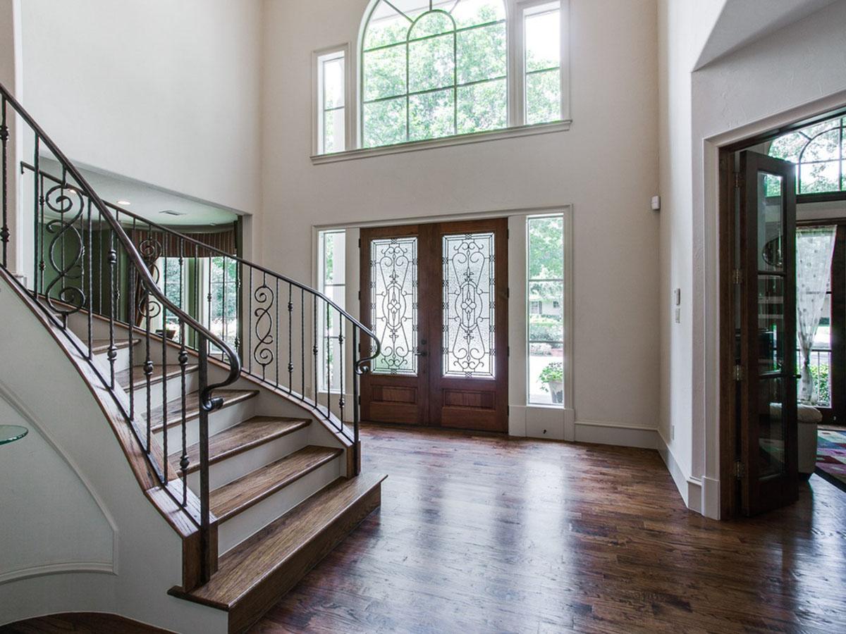 Interior view of house foyer with grand curved staircase, double entry doors with stained glass, and arched transom window.