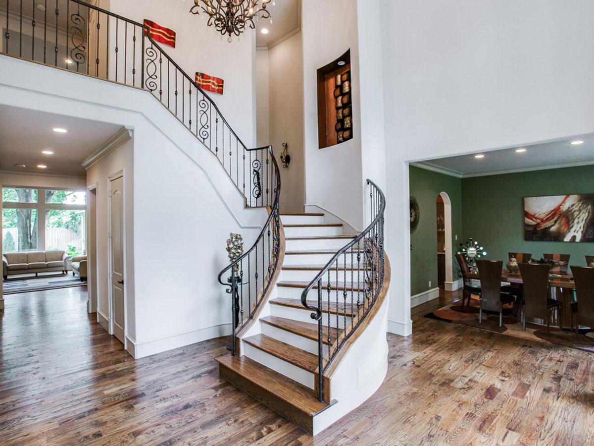 Grand foyer with curved staircase, ornate railing, chandelier, and view into living and dining rooms.