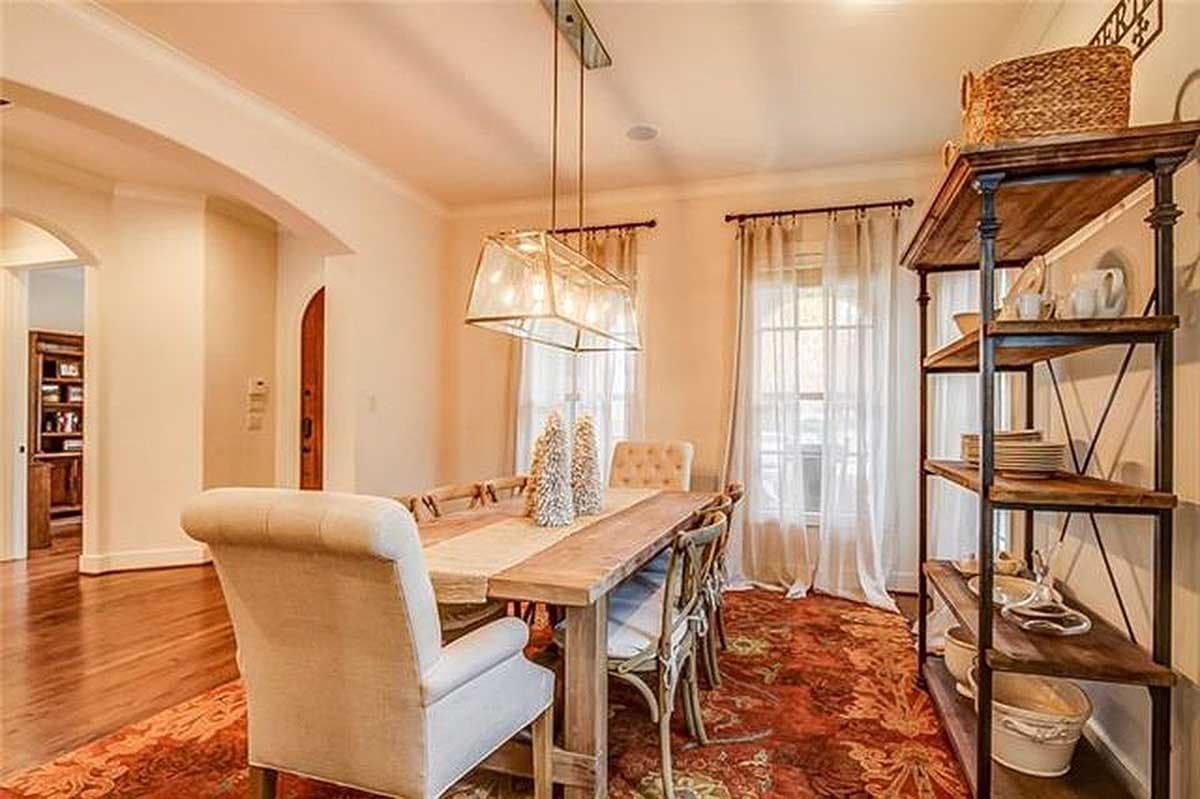Dining room with wooden table, upholstered chairs, large rectangular chandelier, and a tall open shelving unit.
