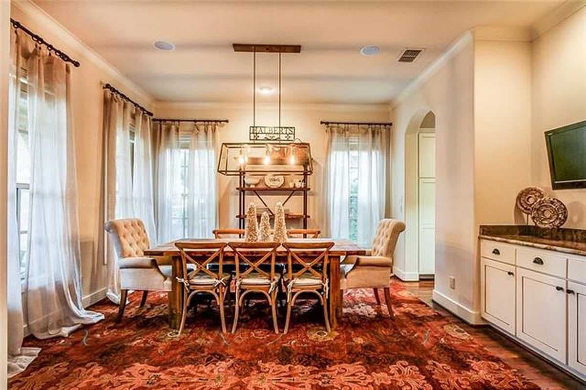 Dining room with wooden table, upholstered chairs, patterned rug, arched doorway, and built-in cabinetry.