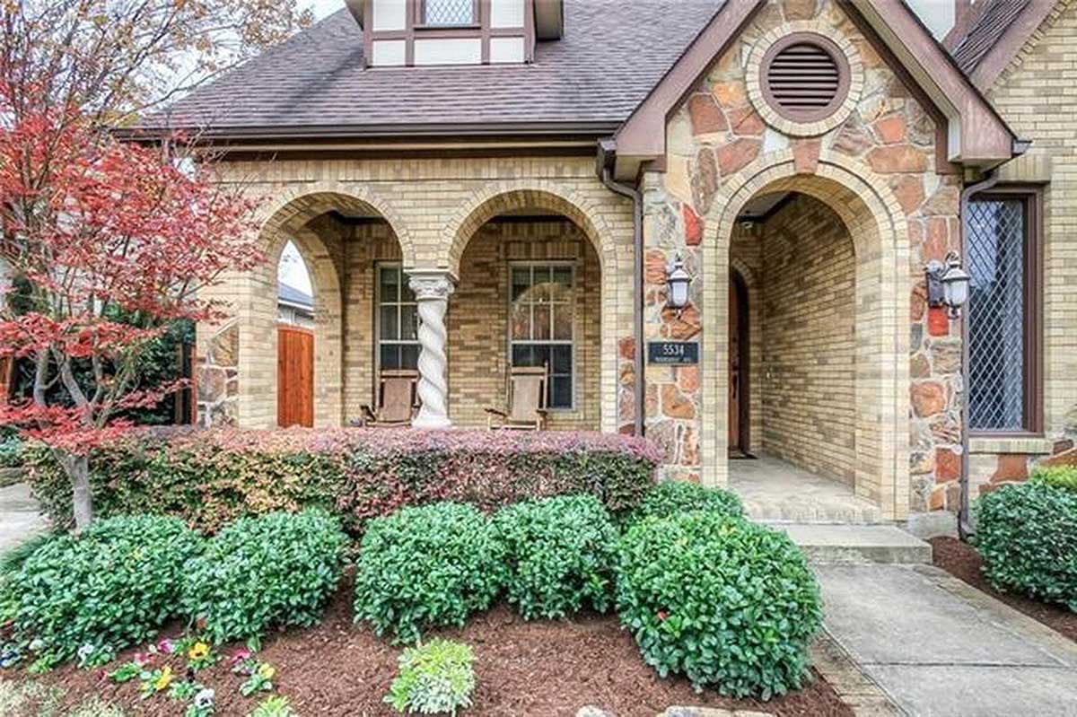 House plan exterior with arched entry, stone accents, and multiple gables. Features a decorative column and dormer window.