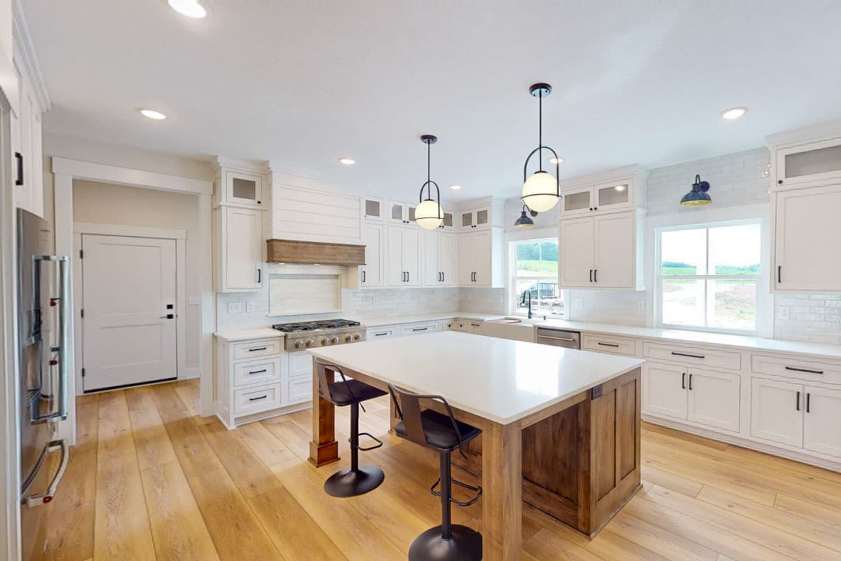 Kitchen with white shaker cabinets, large island with wood base, stainless steel range, and farmhouse sink.