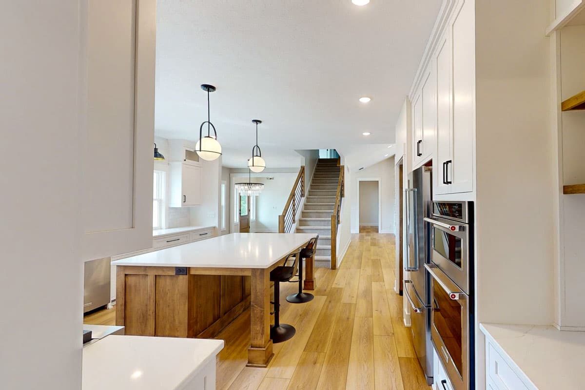 Kitchen and great room with island, stairs, white cabinets, wood floors, and pendant lighting.