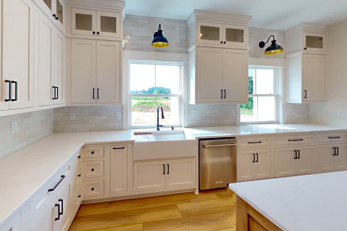 Kitchen interior with white cabinetry, apron sink, stainless steel dishwasher, and subway tile backsplash.
