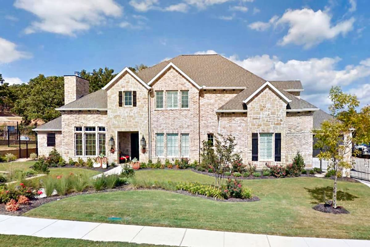 House plan exterior with two stories. Features include multiple gables, stone facade, and shuttered windows. A brick chimney is visible.