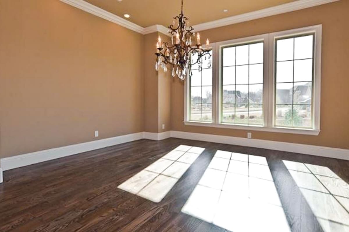 Interior view of an empty room with hardwood floors, a chandelier, and three large grid-pattern windows.