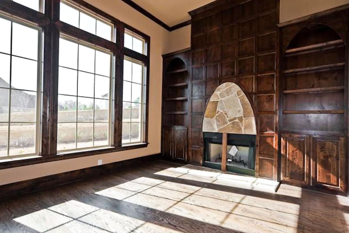 Living room with large grid windows, stone fireplace surround, built-in wood bookshelves, and dark wood flooring.