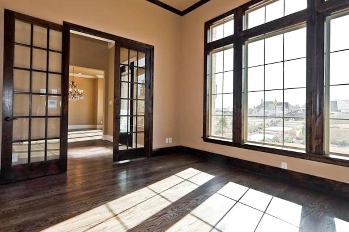 Interior view of a room with dark wood double French doors leading to another space, and a large grid window.