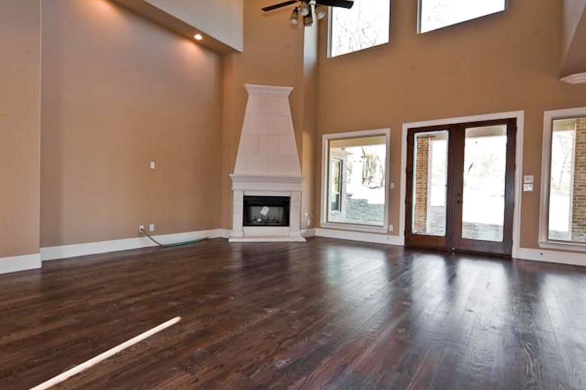Interior view of a great room with a tall, tiled fireplace, vaulted ceiling, and double doors leading outdoors.