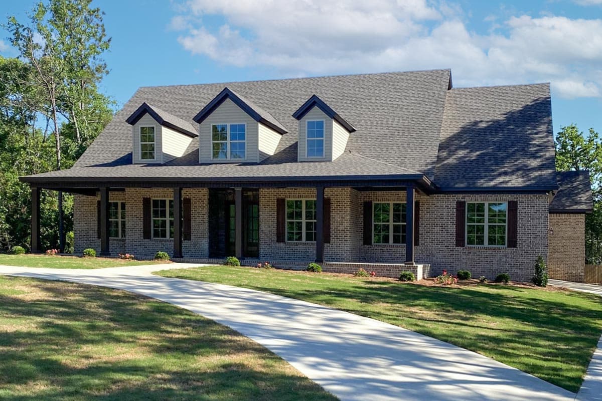 House plan exterior: Traditional one-story brick home with a wide covered porch, three gables, and dark wood shutters.