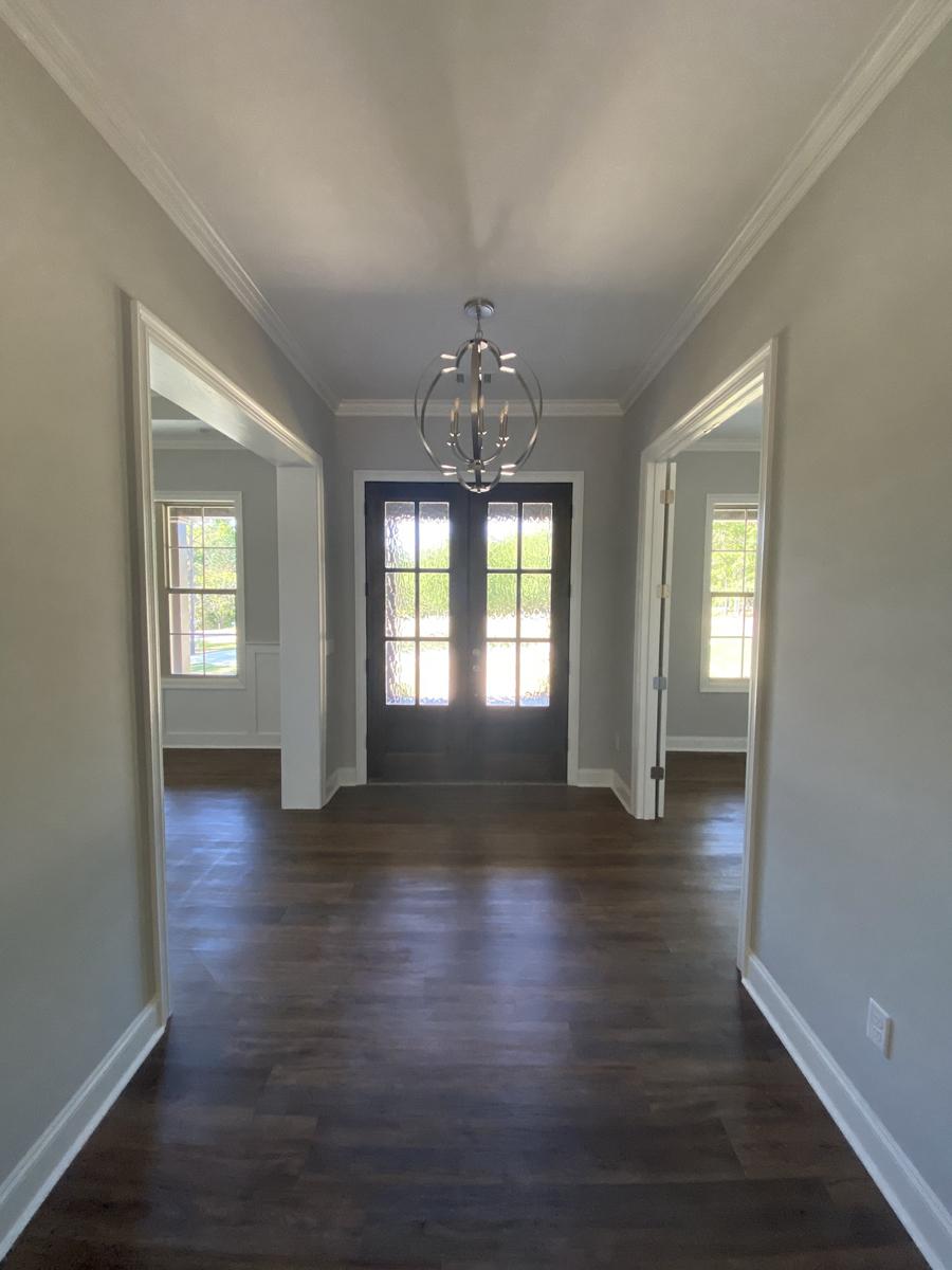 Interior view of a home entryway with dark wood flooring, double glass doors, and a modern chandelier.