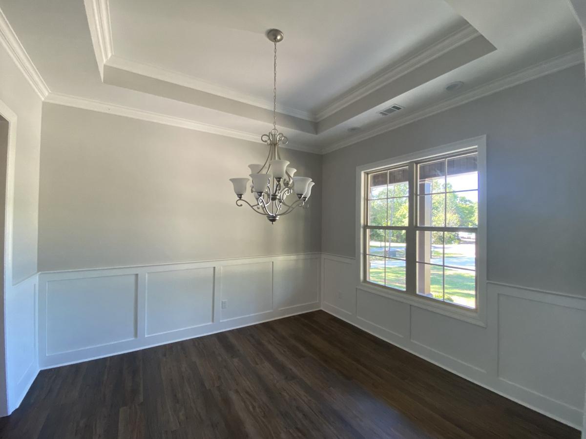 Interior view of dining room with tray ceiling, wainscoting, dark wood floors, and a large window.