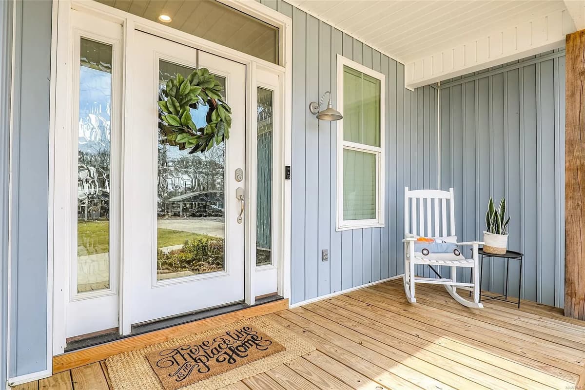 House plan exterior featuring a light blue vertical siding, double glass entry doors with a wreath, and a covered porch with a rocking chair.
