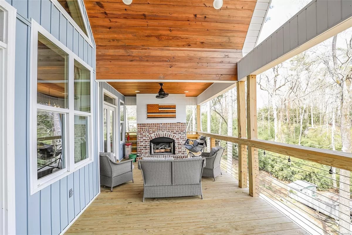 Covered porch with wood plank ceiling, brick fireplace, ceiling fan, and outdoor seating.