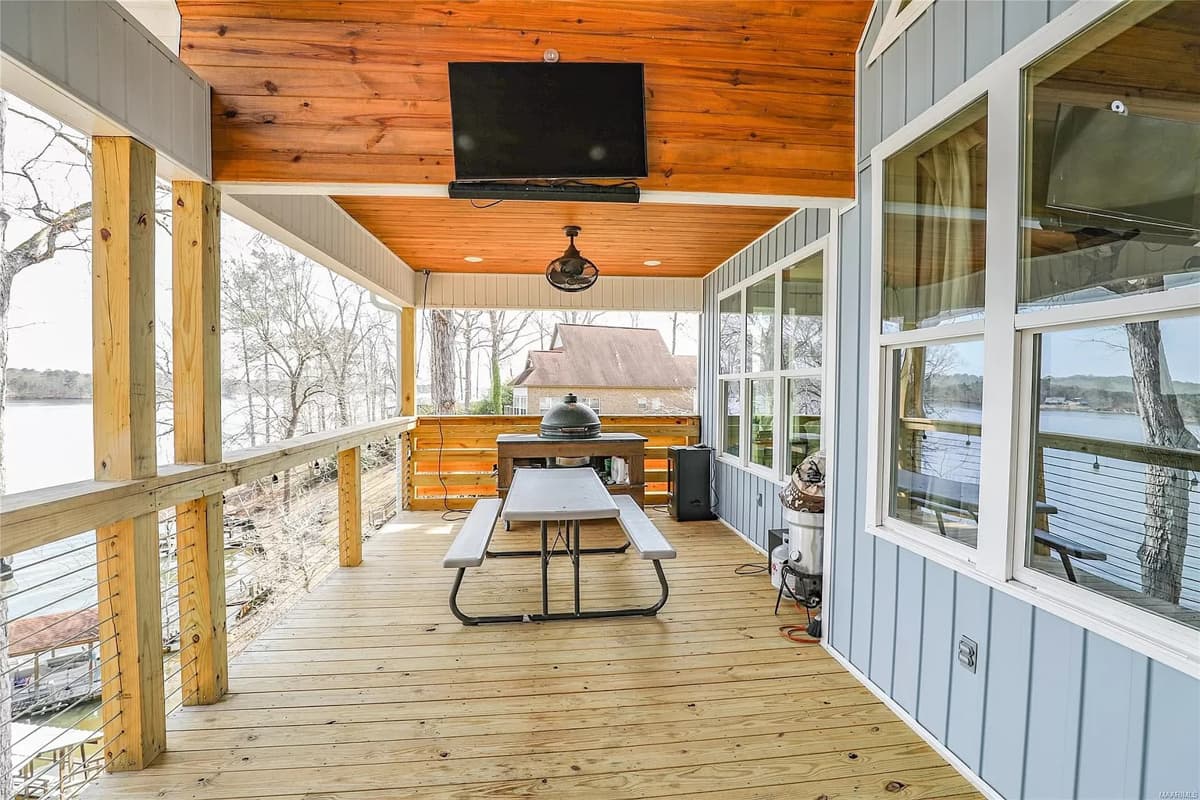 Covered porch with wood ceiling, picnic table, grill, and water view.