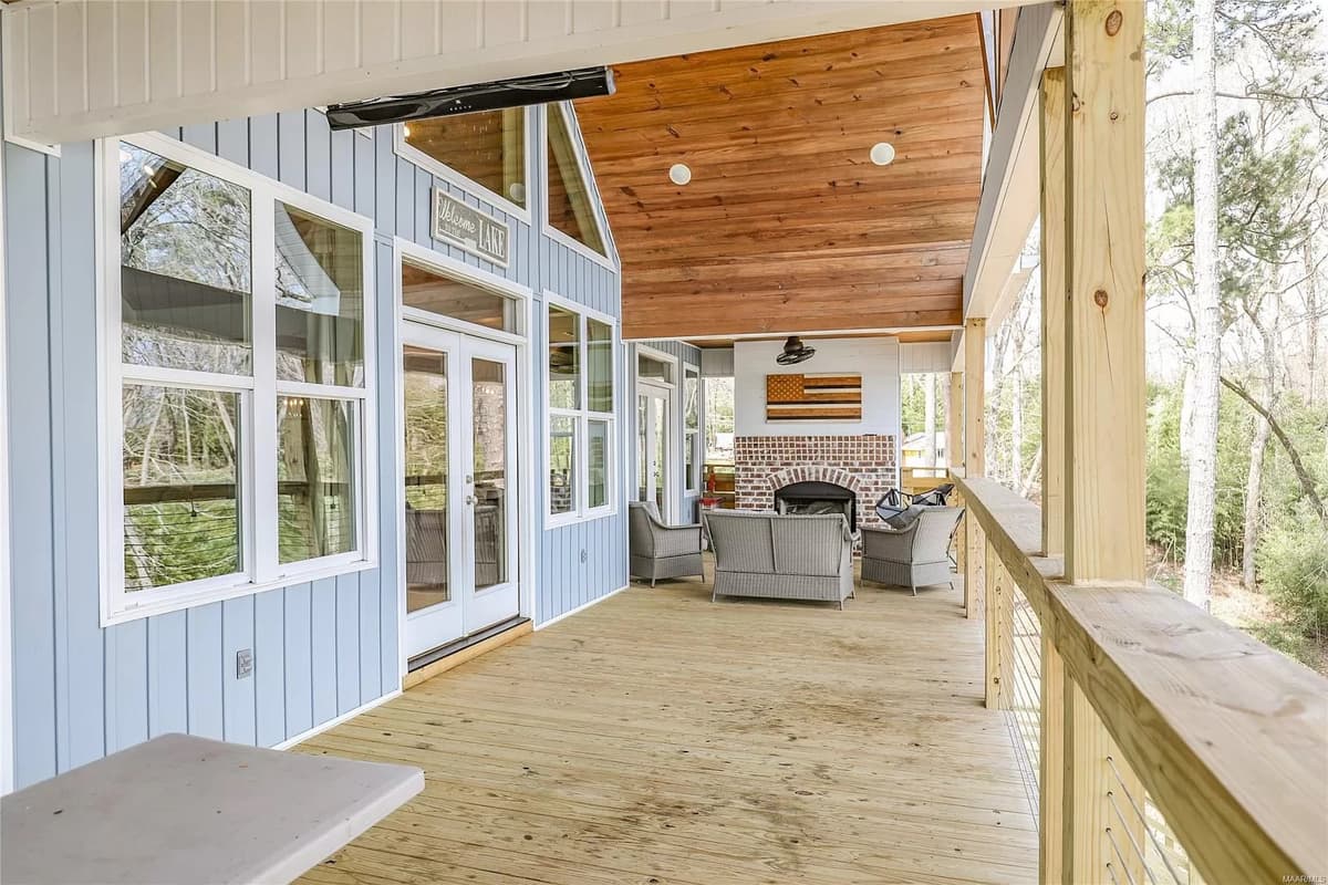 Covered deck with light blue siding, French doors, large windows, wood ceiling, and brick fireplace.