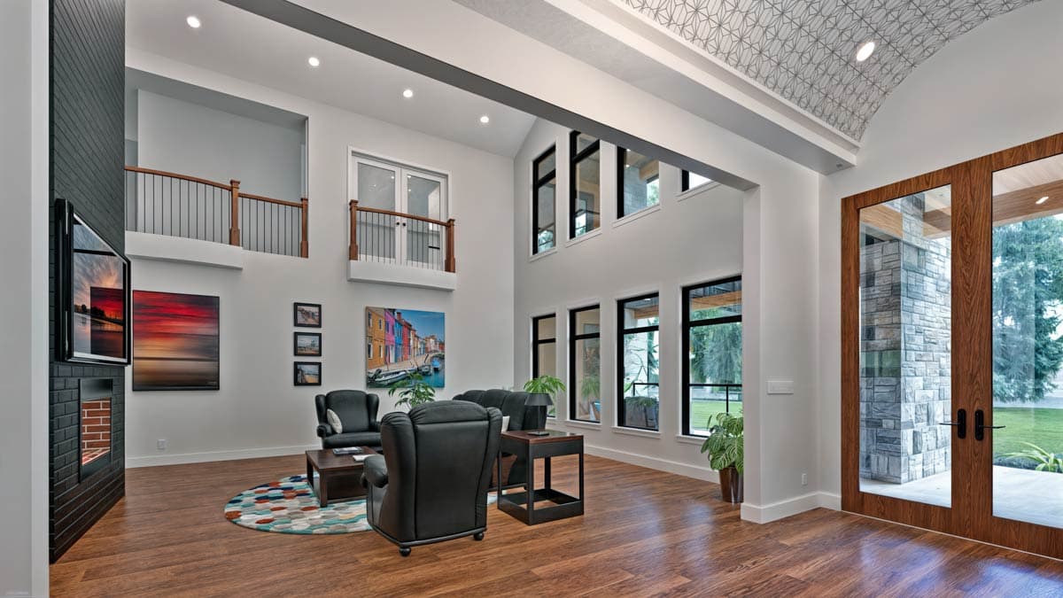 Interior view of a great room with a black brick fireplace, vaulted ceiling, multiple windows, and a second-story balcony.