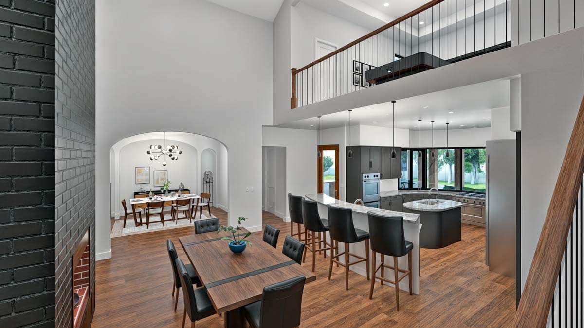 Open concept living area with a vaulted ceiling, dining room, kitchen island with bar stools, and a loft overlooking the space.