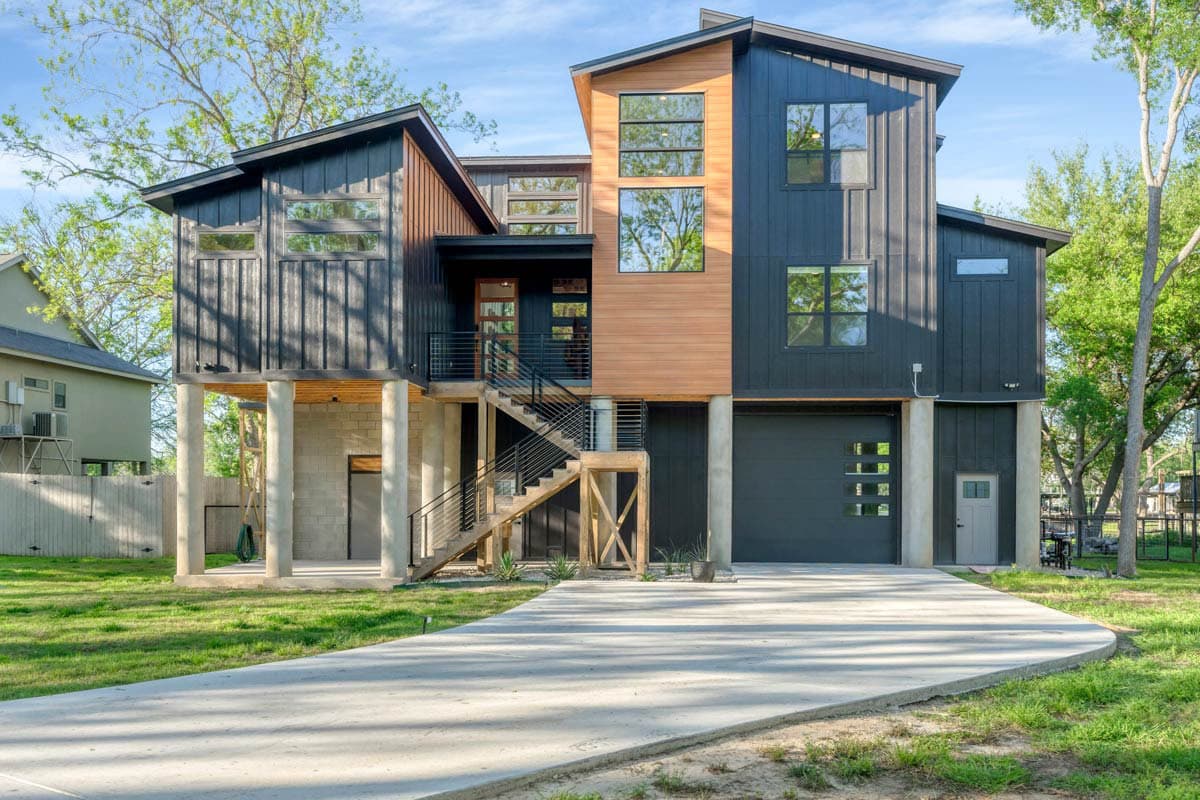 Modern house plan exterior with dark vertical siding, wood accents, multiple gables, and elevated living spaces on stilts.